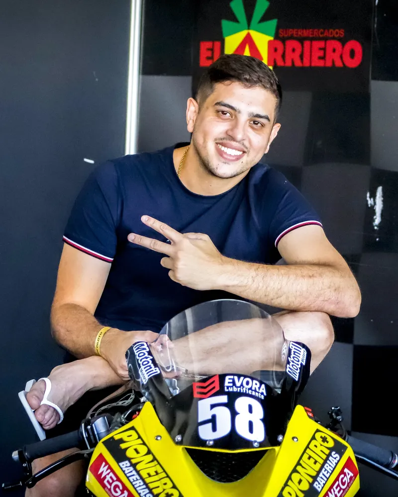 Gustavo Gão sorrindo sentado na moto de número 58 no boxe